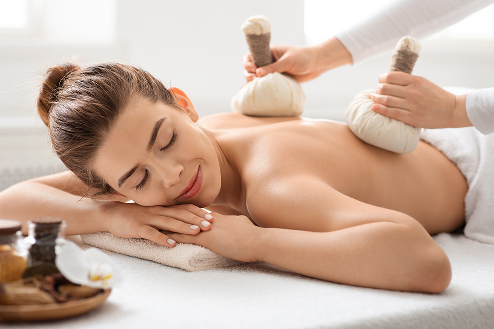 Healing herbal massage. Masseuse making relaxing body massage to young joyful woman with herbal compress balls, spa interior. Closeup of beautiful lady enjoying thai massage with aromatherapy